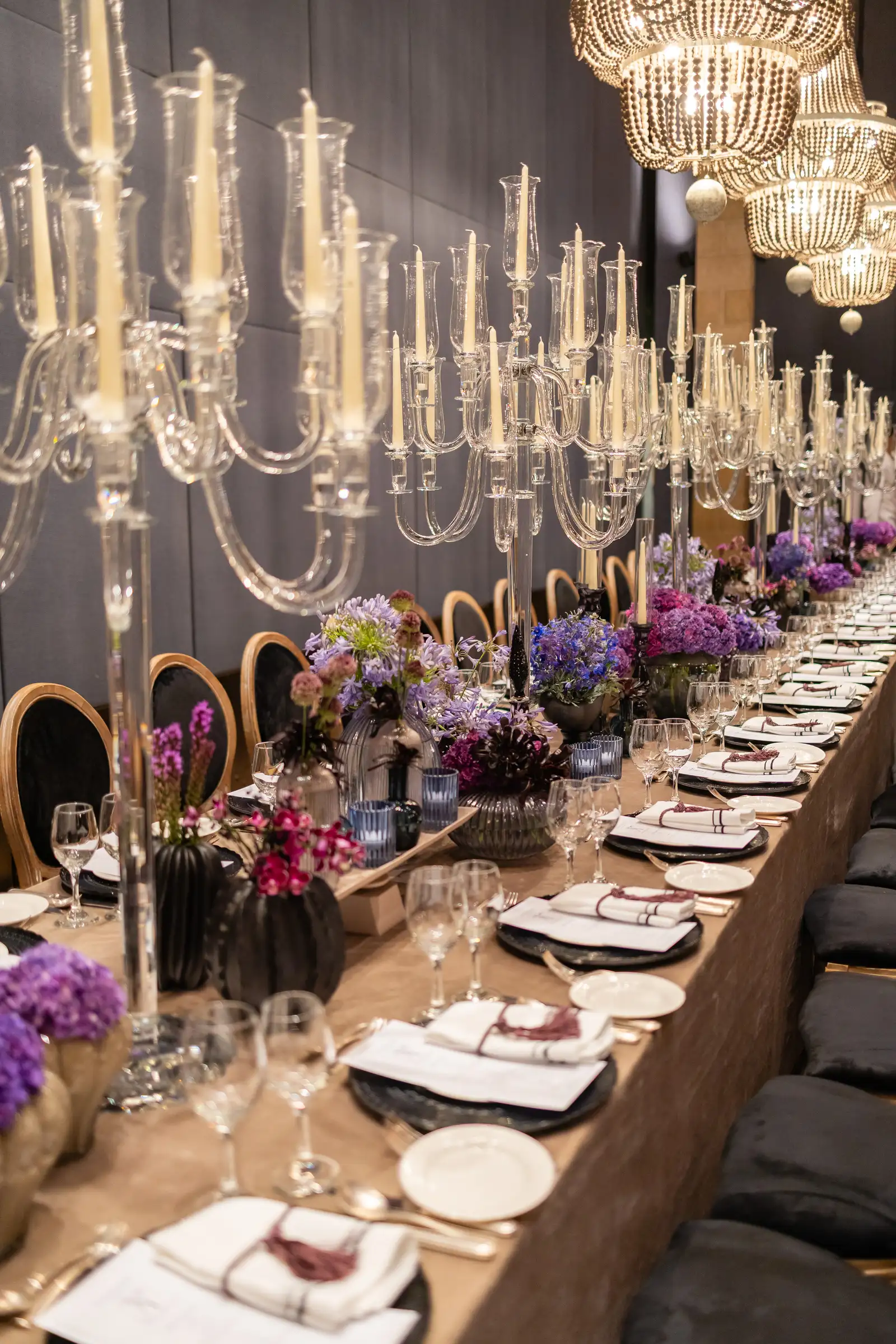 Long table with chandeliers and purple floral arrangements